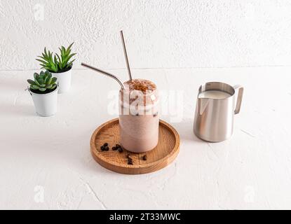 Köstlicher aromatischer frisch gebrühter Kaffee in einem Glasglas in Form einer Bierdose mit Öko-Strohständern auf einem Holztablett. Weißer Hintergrund Stockfoto