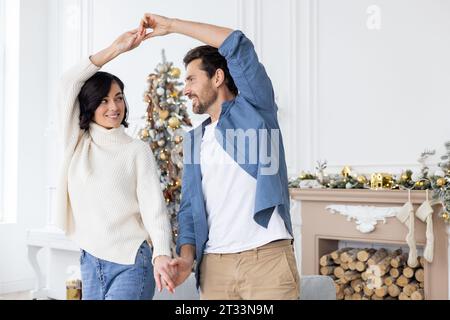 Junge verheiratete Paare Mann und Frau feiern Silvester und weihnachten zusammen, tanzen im Wohnzimmer des Hauses nahe dem Weihnachtsbaum und umarmen lächelnd. Stockfoto