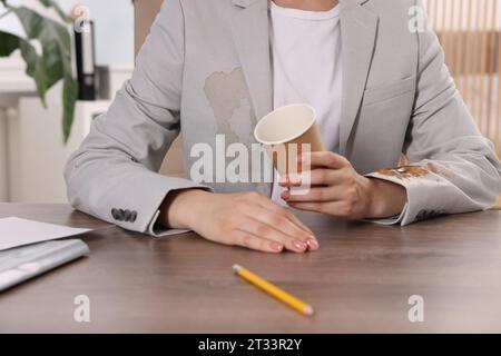 Frau zeigt Flecken von Kaffee auf ihrer Jacke an Holztisch drinnen, Nahaufnahme Stockfoto