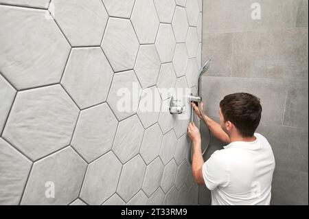 Mann Klempner, der Handbrause im Badezimmer installiert. Männlicher Arbeiter, der Metallduschkopf repariert und Sanitäranlagen während der Renovierung von Häusern erledigt. Stockfoto