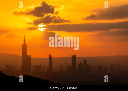 In der Abenddämmerung bricht die Sonne durch die Wolken und scheint auf Taipeh City. Silhouetten von Stadtgebäuden. Orangefarbener Himmel und dunkle Wolken. Stockfoto