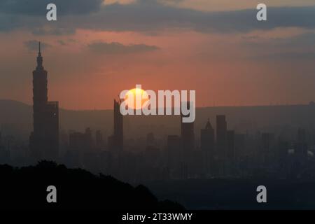 In der Abenddämmerung bricht die Sonne durch die Wolken und scheint auf Taipeh City. Silhouetten von Stadtgebäuden. Orangefarbener Himmel und dunkle Wolken. Stockfoto