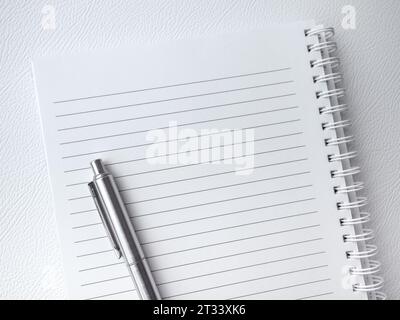 Draufsicht des leeren leeren Leers der Notizbuchseite. Vorlage weißes Papierblatt mit Linie für Notiz auf vertikalem spiralförmigem Notizblock mit einem silbernen Stift isoliert auf Stockfoto