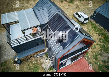 Elektriker, die Kabel anschließen, während Photovoltaik-Solarpaneele auf dem Dach des Hauses installiert werden. Luftaufnahme der Montage des PV-Solarmoduls auf dem Dach von Mounters. Konzept alternativer und erneuerbarer Energien. Stockfoto