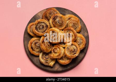 Frisch gebackene süße und knusprige Zimtrollen. Auf einem Holzteller und rosa Hintergrund Stockfoto