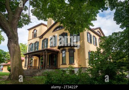 Blick nach oben zur gelben Veranda und zum Turm des Seward House durch die Blätter eines großen Baumes an einem hellen Sommertag in Auburn, New York. Stockfoto