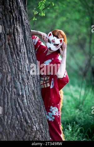 Das Mädchen in einer Maske blickt hinter einem Baum raus Stockfoto