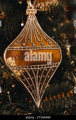 Goldenes Weihnachtsspielzeug mit Text Love and Live hängt am Baum. Goldene Bokeh-Lichter auf festlichem Hintergrund Stockfoto