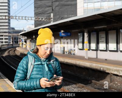 Rucksacktouristenfrau mit Handy am Bahnhof Stockfoto