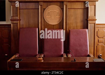 Drei karmesinrote Lederstühle stehen am Holztisch mit Hammer, Mikrofon und schwarzem Ordner mit juristischen Dokumenten im Gerichtssaal Stockfoto