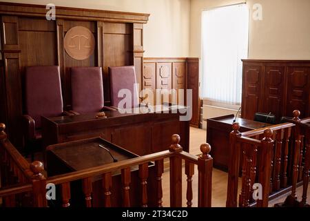 Teil des geräumigen Gerichtssaals mit Holzmöbeln und Lederstühlen für Richter, die an ihrem Schreibtisch mit Mikrofon und Hammer stehen Stockfoto