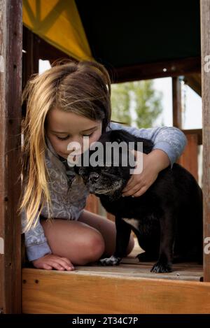 Kleines Mädchen umarmt schwarzen Mops Hund im Spielhaus Stockfoto