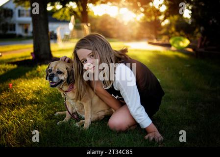 Ein junges Mädchen sitzt mit lächelndem und keuchender Puggellhund im Hinterhof Stockfoto