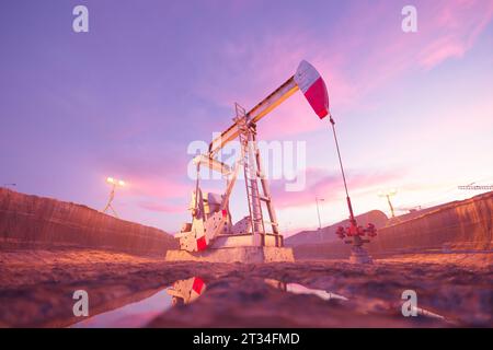 Pumpjack in überfluteter Ausgrabung voller Schlamm. Täglich und abends arbeitende petrochemische Ausrüstung auf dem Ölfeld am Sonnenuntergang. Suppor Stockfoto