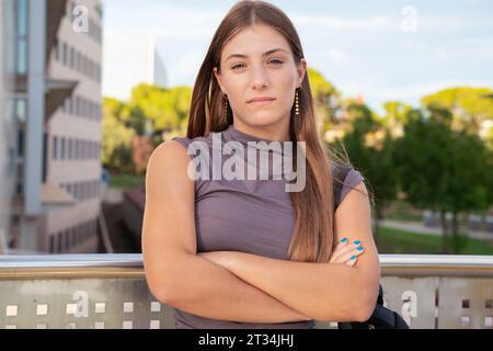 Porträt Junge ernsthafte kaukasische Studentin mit überkreuzten Armen, die im Freien nachdenklich aussieht. Stockfoto