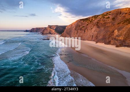 Wellen des Atlantiks an der Küste, Sandstrand und dramatische Klippen in Portugal. Drohnenansicht aus der Luft Stockfoto