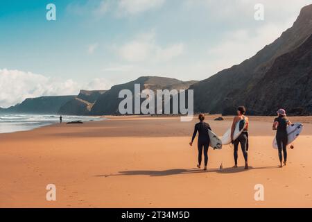 Junge Surfer, die am Sandstrand am Atlantischen Ozean in Portugal mit Surfbrettern spazieren gehen. Stockfoto