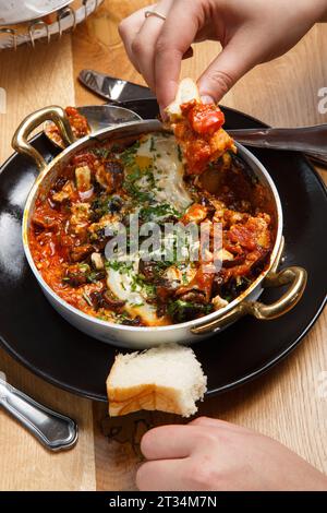 Shakshuka mit Brot in einer Pfanne. Essen. Traditionelles Gericht aus dem Nahen Osten. Spiegelei mit Tomaten, Paprika, Gemüse und Kräutern. Shakshouka auf einem T Stockfoto