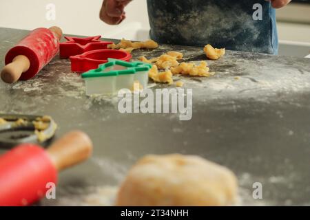 Kleiner kleiner Junge, der zu Hause Weihnachtskekse backt. Roter Pin- und Keksschneider auf dunkelgrauem Küchentisch. Stockfoto