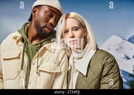 Attraktives Paar in stilvollen modernen Outfits mit verschneiten Bergen im Hintergrund, Winterkonzept Stockfoto