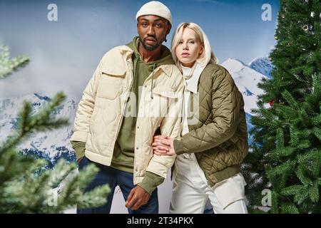 Stilvolles, multirassisches Paar in warmer Winterkleidung, das sich vor verschneiten Kulissen ausstellt, Modekonzept Stockfoto