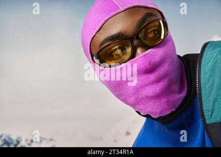 Porträt eines jungen afroamerikanischen Mannes in rosa, lebendiger Sturmhaube, der wegblickt, Winterkonzept Stockfoto