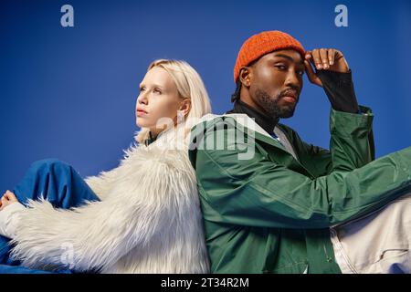 Interrassische Models in trendigen Winteroutfits, die sich vor blauem Hintergrund, Vielfalt und Stil präsentieren Stockfoto