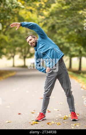 Ein junger Athlet wärmt sich vor dem Lauftraining im Park auf. Sie erwärmt den oberen Teil des Körpers. Stockfoto