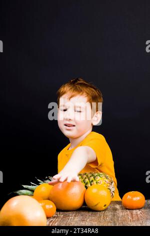 Ein schöner rothaariger Junge mit Zitrusfrüchten, aus denen man Saft oder andere Lebensmittel machen kann, ist der Junge glücklich und isst und spielt mit Zitrusfrüchten Stockfoto