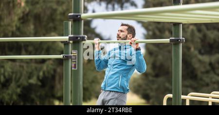 Junger Mann, der Calisthenics in einem Fitnessstudio im Freien mit parallelen Bars ausführt. Er macht Liegestütze an der Bar. Konzept des gesunden Lebensstils. Stockfoto