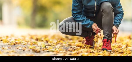 Eine Nahaufnahme der Hände eines Athleten, der seine Schnürsenkel bindet, bevor er in einem Herbstpark läuft. Stockfoto