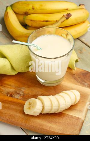 Eine Hand Bananen, eine geschnittene Banane und ein Glas Milch auf einem hölzernen Küchenbrett Stockfoto