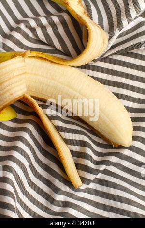 Eine abgeschälte Banane auf einer grau-weiß gestreiften Tischdecke in einem Blick von oben Stockfoto