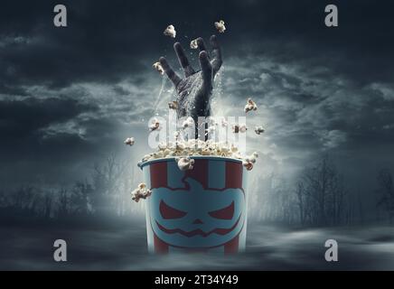 Gruselige Zombie-Hand aus einem Popcorn-Eimer: Horrorfilme und Halloween-Konzept Stockfoto