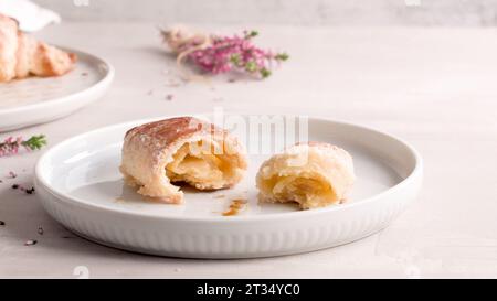 Kleine Croissants auf weißen Keramikplatten, hausgemachte Kuchen auf Betontischplatte. Stockfoto