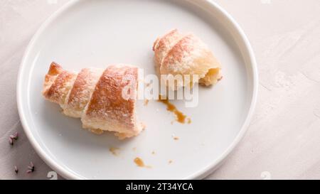 Kleine Croissants auf weißen Keramikplatten, hausgemachte Kuchen auf Betontischplatte. Stockfoto