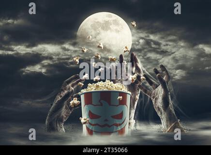 Popcorn-Eimer umgeben von Zombie-Händen und Vollmond: Horrorfilme und Halloween-Konzept Stockfoto