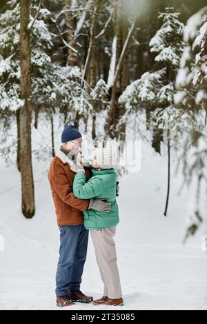 Senior Mann und Frau in Winterkleidung, die sich umarmen und anschauen Stockfoto