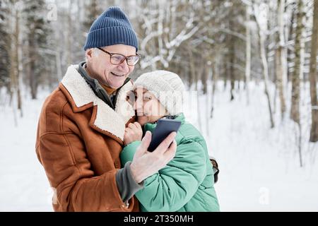 Glückliches, verliebtes Seniorenpaar, das Selfies macht, wenn man im kalten Winter im Park spaziert Stockfoto
