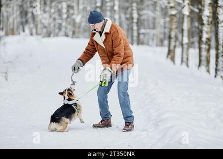 Glücklicher Seniorenmann, der mit Hund im Winterpark spielt Stockfoto