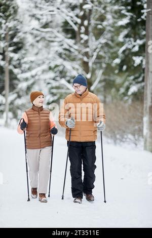 Fröhlicher älterer Ehemann und Ehefrau spazieren mit Trekkingstöcken im Winterwald Stockfoto