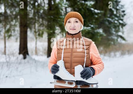 Porträt einer positiven lächelnden Seniorin in warmer Kleidung im Wald mit Schlittschuhen Stockfoto