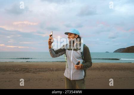 Mann Blogger fotografieren mit Smartphone von Sonnenuntergang Meer Touristen allein reisen Sommerurlaub Lifestyle Outdoor Stockfoto