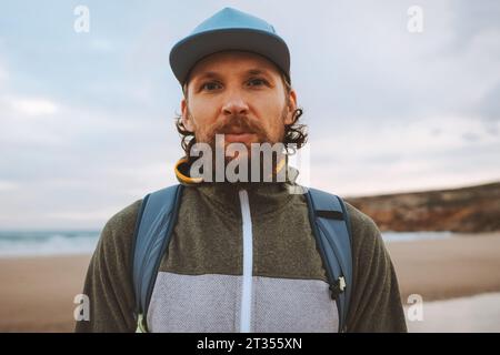 Bärtiger Mann Portrait im Freien brutaler Mann mit Mütze, der mit Rucksack geht, Reise-Lifestyle, aktiver Sommerurlaub Stockfoto