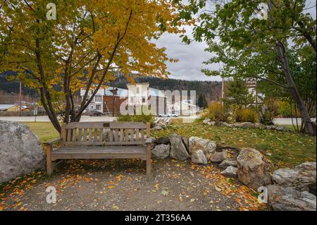Herbstblick auf eine Parkbank mit weit entfernten Gebäuden in Dawson City, Yukon, Kanada Stockfoto