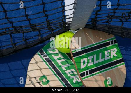 West Islip, New York, USA - 17. Juley 2023: Blick auf zwei Pickleball-Schläger im Tennisnetz mit einem Whistle Ball aus nächster Nähe. Stockfoto