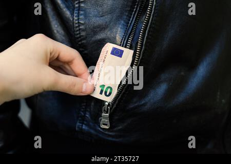 Die Hand zieht Papiergeld und Karte aus der Tasche. Ein Dieb hat einen Mann ausgeraubt. Bargelddiebstahl, kriminelles Konzept. Stockfoto