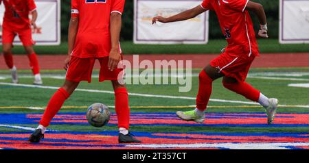 Highschool-Fußballspieler in roten Uniformen, die den Ball während eines Spiels auf einem Rasenfeld an einander weitergeben. Stockfoto