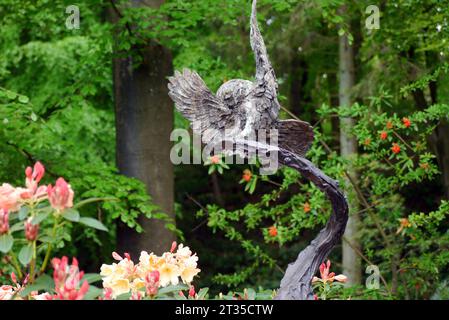 Bronzeskulptur einer Tawny Owl, die auf einem Zweig fliegt, von dem Künstler Hamish Mackie im Himalaya Garden & Sculpture Park, North Yorkshire, England. Stockfoto