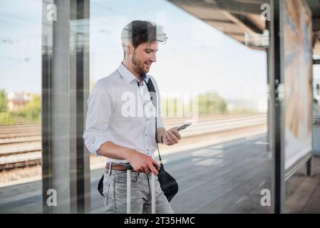 Geschäftsmann mit Gepäck auf Bahnsteig mit Handy Stockfoto